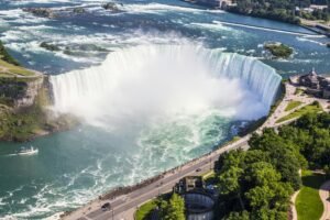 Holiday Tour Packages. Stunning aerial shot of Niagara Falls with a boat tour and lush greenery on a sunny summer day.