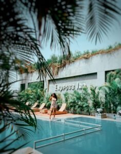 Holiday Inn Woman enjoying a sunny day by the pool at Express Inn surrounded by lush greenery.