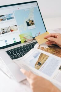 Booking Com Hands holding credit card over laptop and magazine for online shopping and travel planning.